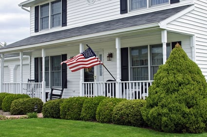 White colonial-style home with farmer's porch and American flag