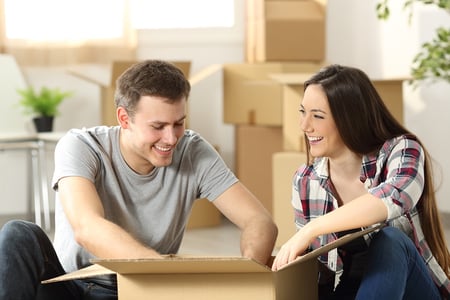 Couple moving home packing belongings in a cardboard box sitting on the floor of the living room in Massachusetts