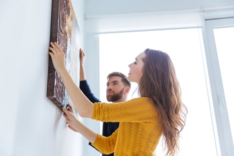 Happy couple hanging picture on the wall of their new home.