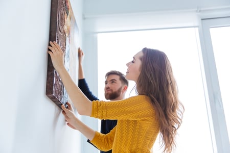 Happy couple hanging picture on the wall of their Massachusetts home. 