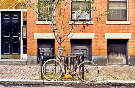 A Beacon Hill brick condo [Boston] with a  bicycle out front near a pumpkin in the late fall.
