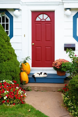 White house with a red door and pumpkin on the steps