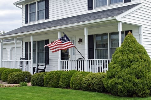 White colonial house with a farmer's porch and an American Flag