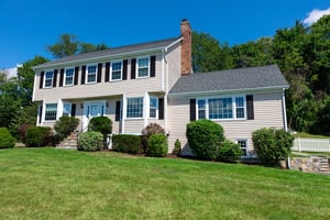 tan colonial-style home with black shutters on a sunny day